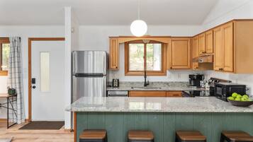 Cocina moderna con armarios de madera, refrigerador de acero inoxidable, encimera de granito y una isla verde con taburetes.