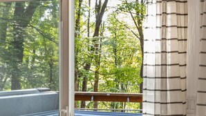 Une pièce dotée d’une porte-fenêtre coulissante donnant accès à un jacuzzi, à une terrasse en bois et offrant une vue sur les arbres.