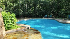 A swimming pool with a curved edge, surrounded by stone steps and greenery. - Wooded Nest, Cozy 3BR Chalet Near Spas & Hiking (Berkeley Springs)
