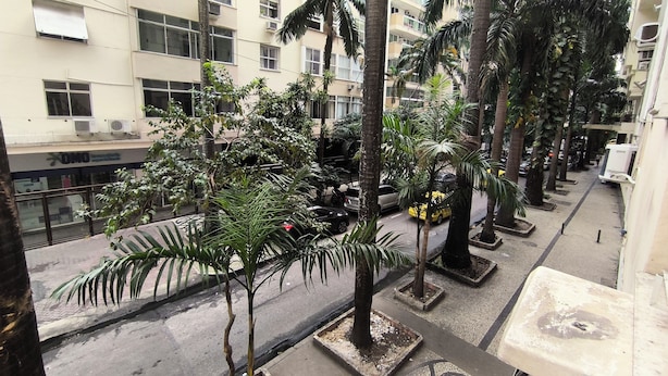 Een meerlaags woongebouw met balkons, airconditioners, een straat met geparkeerde auto's en palmbomen.