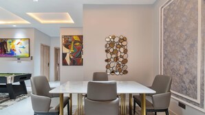 Une salle à manger moderne avec une table blanche et quatre chaises grises, une table de billard et des œuvres d’art abstraites accrochées aux murs.