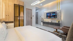 Une chambre d’hôtel moderne avec un grand lit, une armoire en bois, un téléviseur fixé au mur et un petit coin salon.