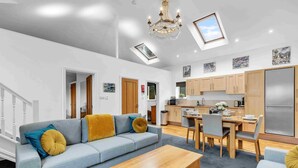 A modern living room with a sofa, coffee table, and dining area. There is a kitchen with wooden cabinets and a refrigerator. - Garden Lodge With Parking  | By My Getaways (Brighton)