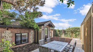 A patio area with a wooden table and chairs, a brick wall, and a window. - Garden Lodge With Parking  | By My Getaways (Brighton)