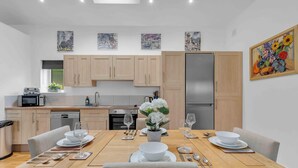 A modern kitchen with wooden cabinets, a stainless steel refrigerator, and a dining area with a wooden table set for four. - Garden Lodge With Parking  | By My Getaways (Brighton)