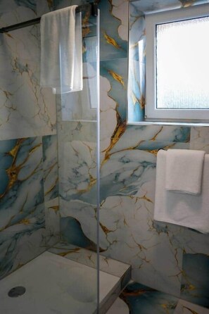 A bathroom with a glass shower enclosure, marble walls, and a window. - Bright 3-Room Apartment ,Terrace, Wi-Fi & Parking – Families & Business Guests🌟 (Garbsen)