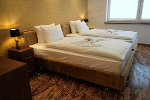 A double bed with white linens, a bedside table with a lamp, and a wooden floor.