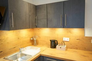 A kitchen with dark cabinets, a wooden countertop, a stainless steel sink, a kettle, and a spice rack.