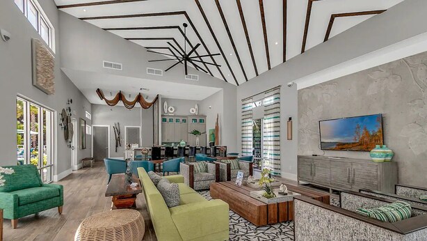 A spacious living area with a high ceiling, modern furniture, and a large TV. - Beautiful Disney Home! Heated Pool/Spa • Arcade • Gated Community • 4BR / 3BA (Kissimmee)
