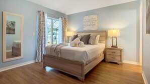 A bedroom with a bed, bedside tables, a mirror, and a window with curtains. - Beautiful Disney Home! Heated Pool/Spa • Arcade • Gated Community • 4BR / 3BA (Kissimmee)