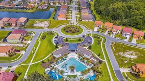 An aerial view of a residential area with a central swimming pool surrounded by houses, roads, and greenery. - Beautiful Disney Home! Heated Pool/Spa • Arcade • Gated Community • 4BR / 3BA (Kissimmee)