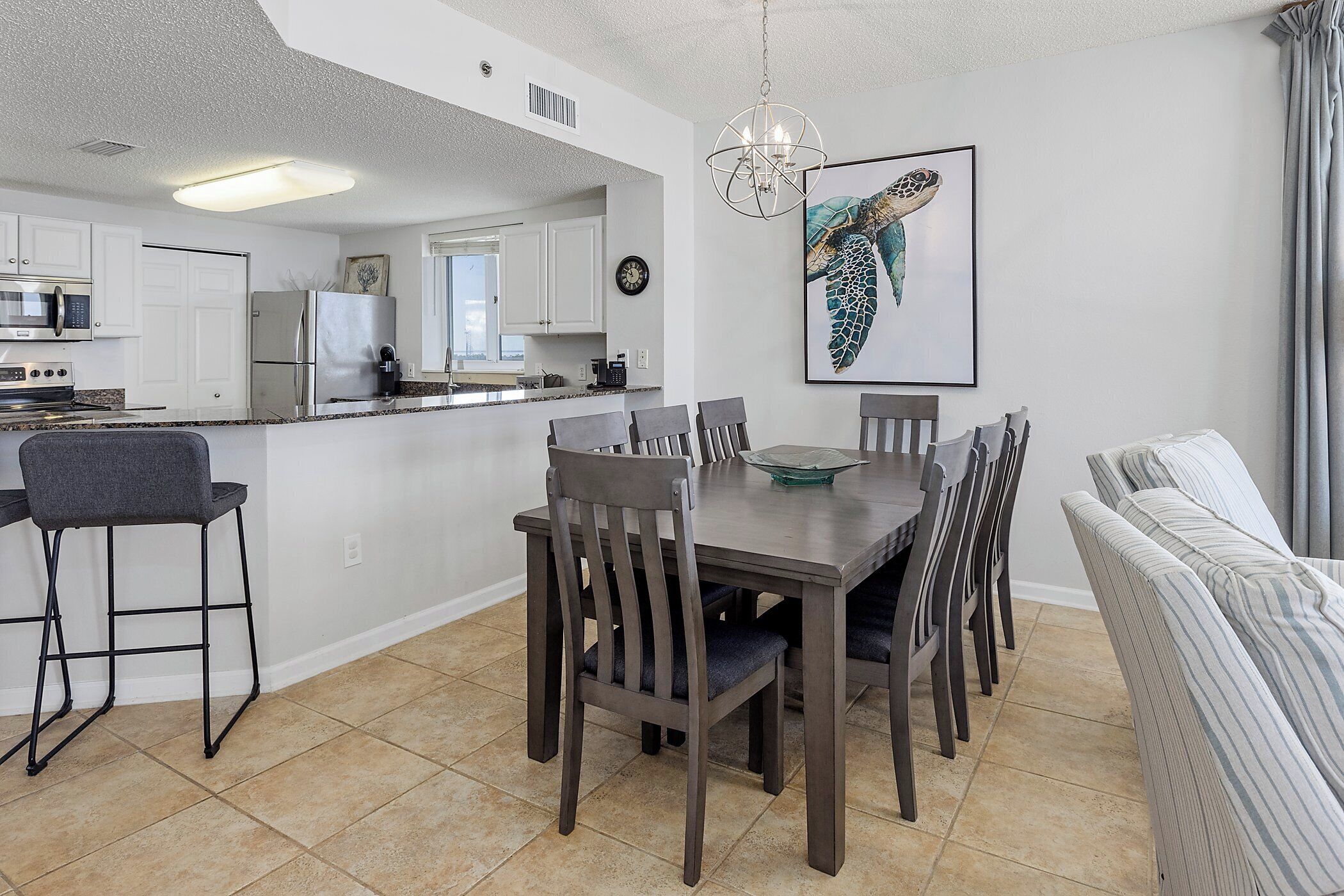 A modern kitchen with white cabinets, a stainless steel refrigerator, and a dining area with a wooden table and chairs.