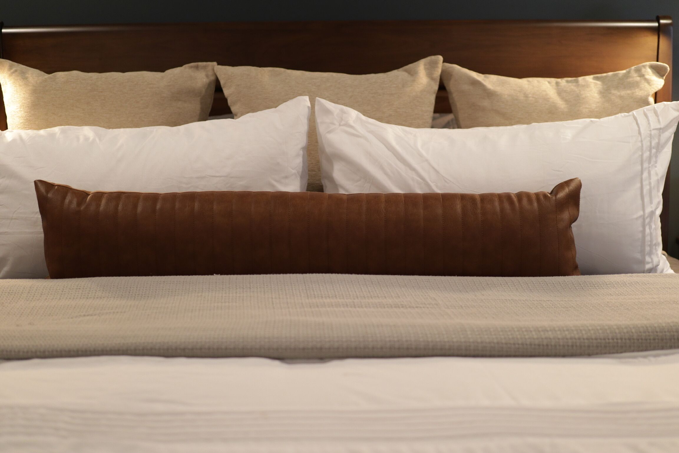 Un letto rifatto con precisione, con un cuscino marrone e cuscini bianchi, una testiera in legno e una coperta bianca con trama.
