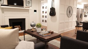 A living room with a fireplace, a coffee table with books and a vase, and a guitar on the wall. - Wanderlust With Us (Atlanta)