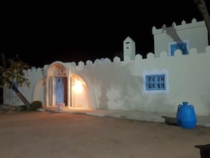 A building with a white exterior, a small arched entrance, and a blue sign with Arabic script.