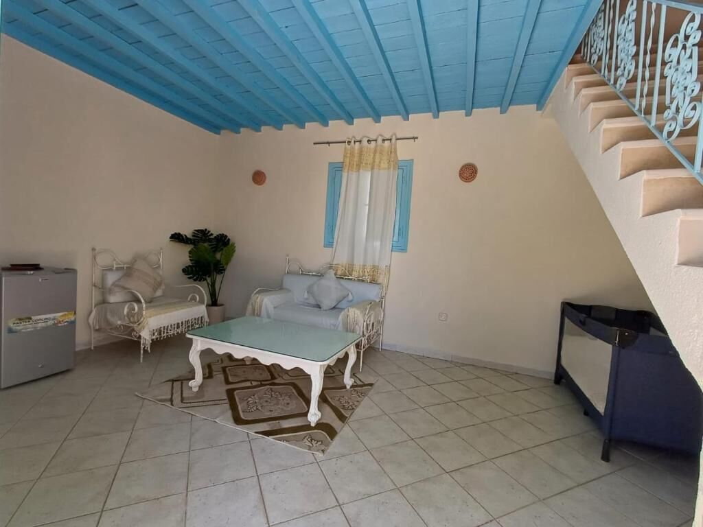 A living room with a blue ceiling, a sofa set, a coffee table, a staircase, and a small table with a plant.