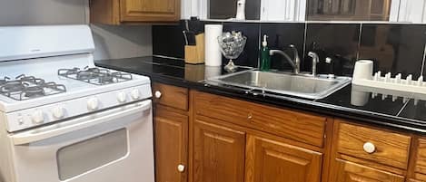 A kitchen with wooden cabinets, a white stove, a black countertop, and a window above the sink.