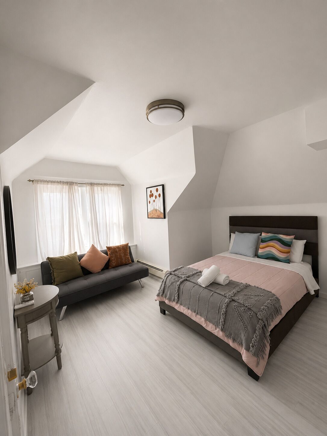 A modern bedroom with a bed, a sofa, a small table, and a painting on the wall.