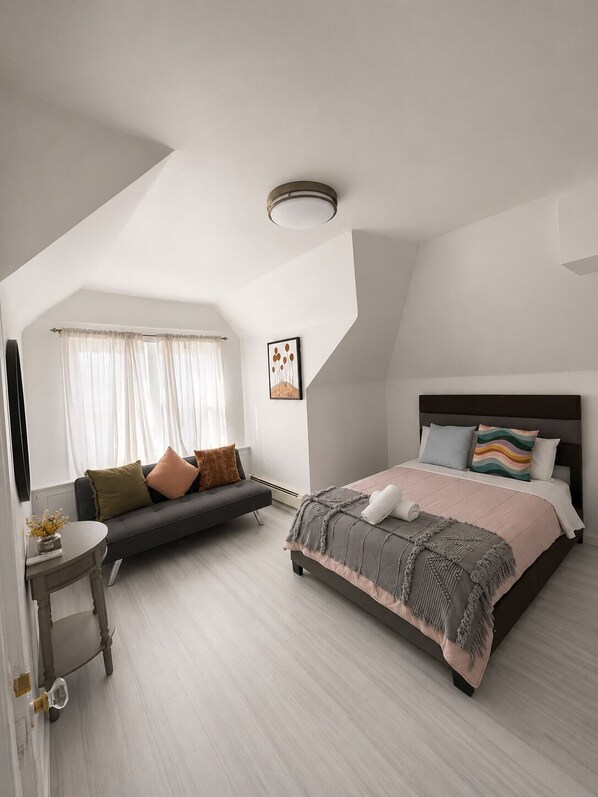 Un dormitorio moderno con una cama, un sofá, una mesita y un cuadro en la pared.