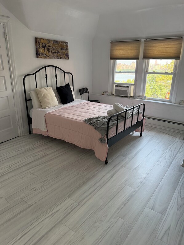 A bedroom with a bed, a chair, a window with blinds, and a painting on the wall.