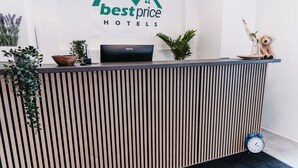 Un mostrador de recepción con el logotipo de Best Price Hotels, un monitor BenQ, un reloj y un peluche.