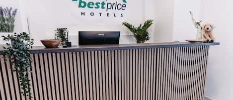 Una recepción con el logotipo de Best Price Hotels, un monitor BenQ, una figurita de perro y un reloj.