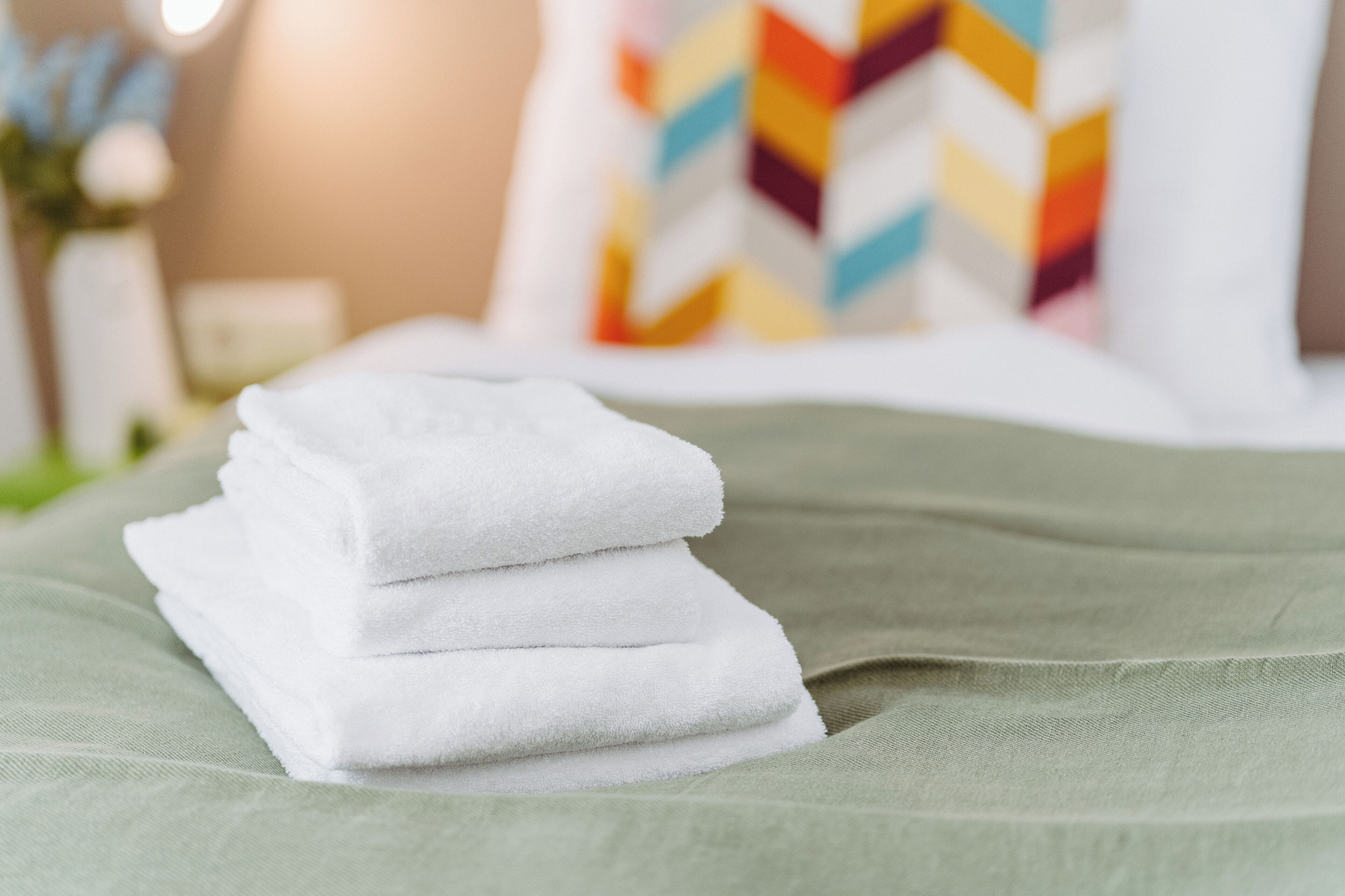 A neatly folded stack of white towels on a green bedspread.