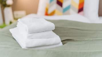 A neatly folded stack of white towels on a green bedspread.