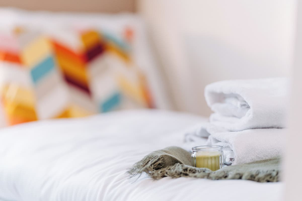 A neatly made bed with a folded white towel and a glass of water on a textured blanket.
