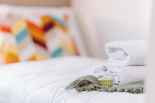 Una cama bien hecha con una toalla blanca doblada y un vaso de agua sobre un edredón texturizado.