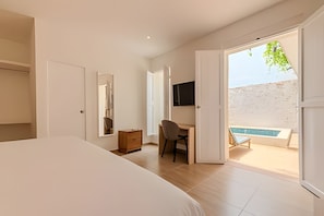 A bedroom with a large bed, a desk with a chair, a TV, and a door leading to a balcony with a pool. - Casa Encanto - Heart of Getsemaní (Cartagena de Indias)