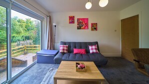A modern living room with a grey sofa, a wooden coffee table, and a large window offering a view of a garden.