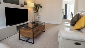 Una sala moderna con un televisor de pantalla plana, una mesa de centro de vidrio, un sofá de cuero blanco y una planta en maceta.
