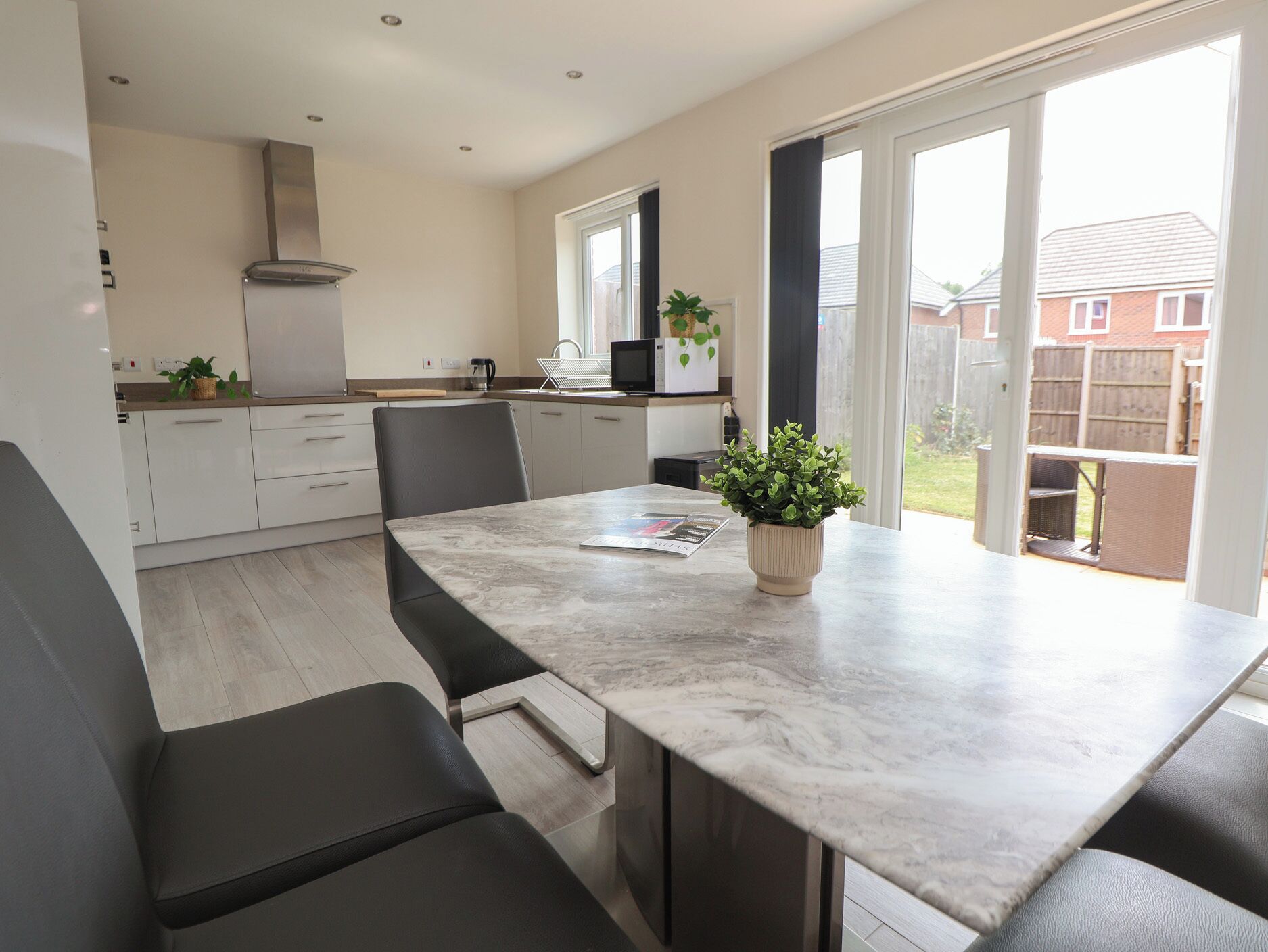 A modern kitchen with a marble countertop, black chairs, and a potted plant.