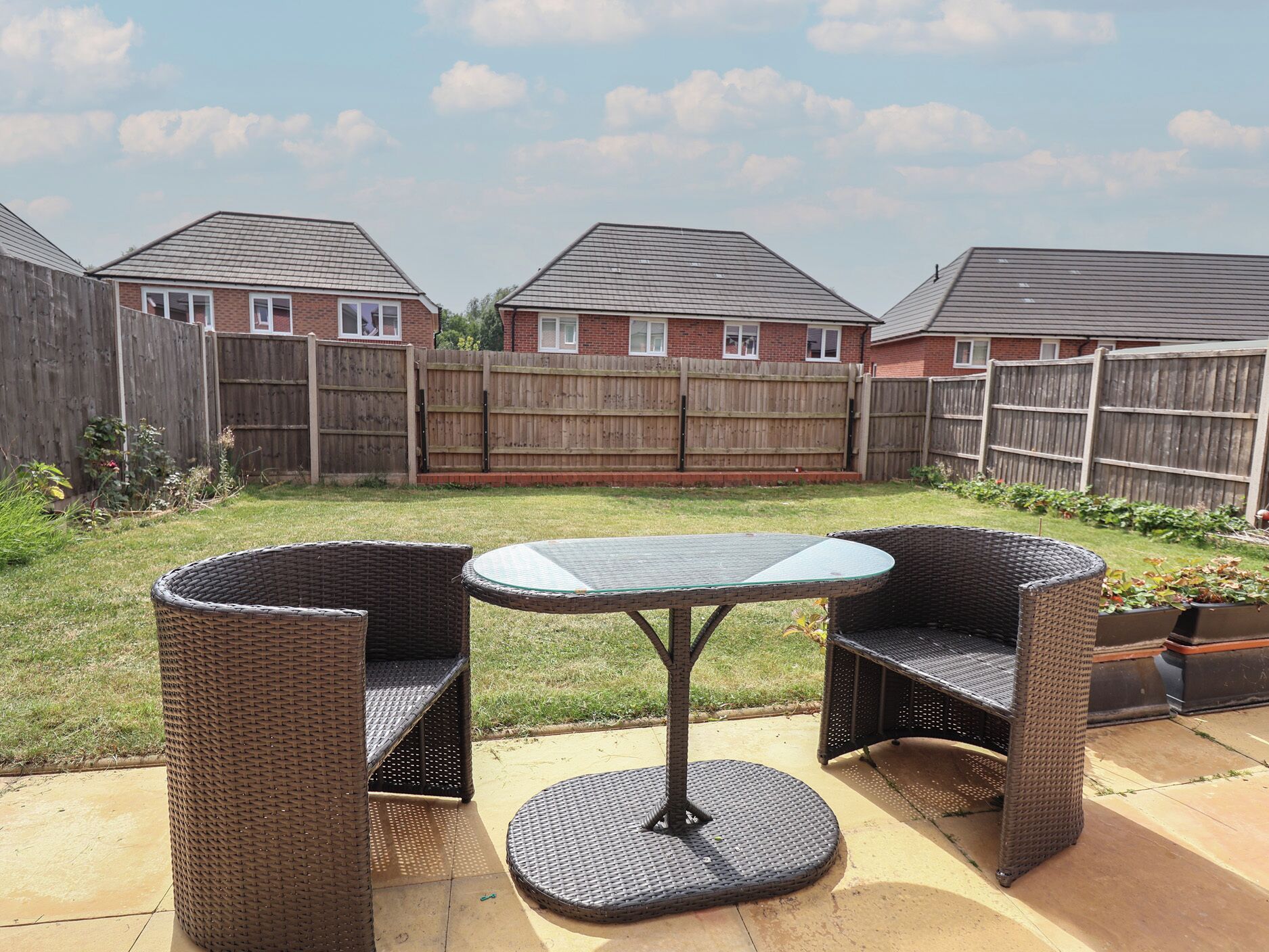 An outdoor patio with wicker furniture, a glass table, and a concrete floor.