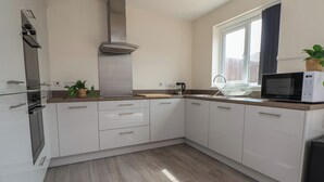 Una cocina moderna con armarios blancos, una campana extractora de acero inoxidable, un microondas y una ventana que proporciona luz natural.