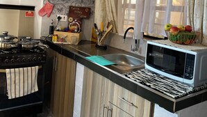 A kitchen with wooden cabinets, a stove, a microwave, and a sink. - Casa Verde – Your Serene Escape in the Heart of Karen (Nairobi)