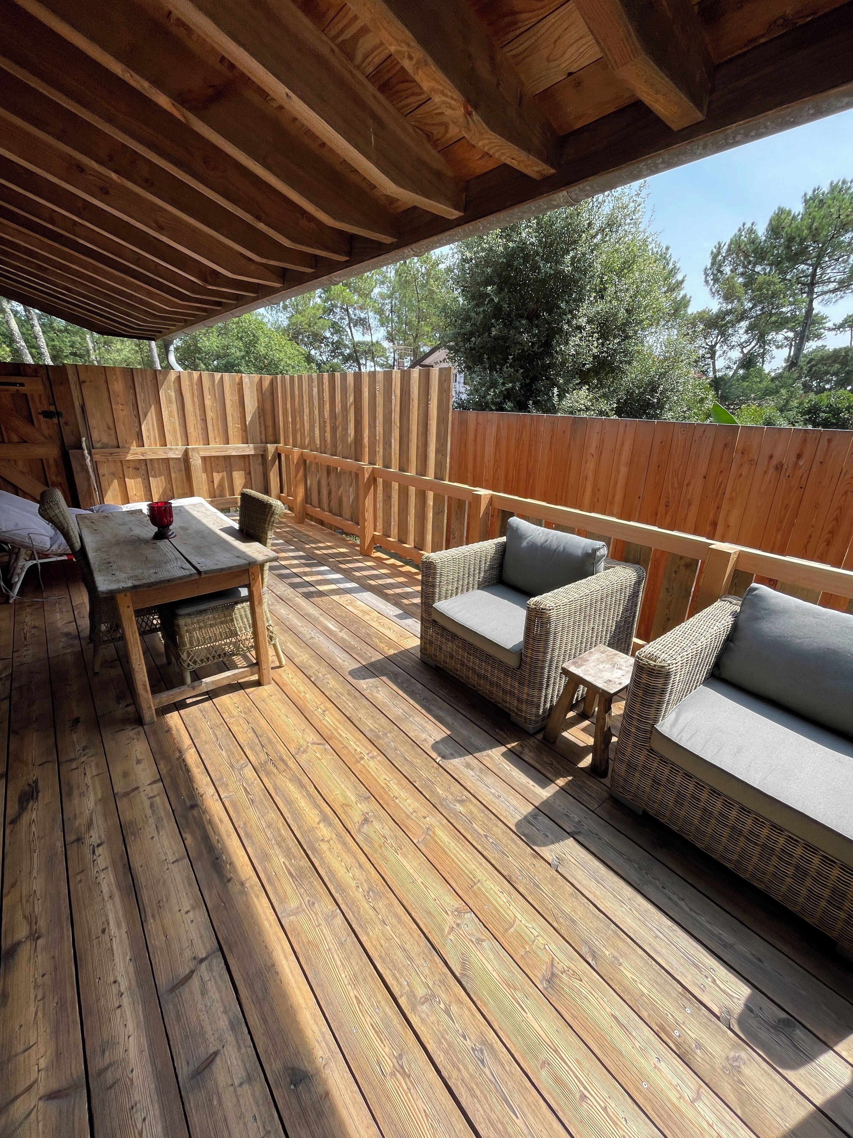 An outdoor wooden deck with a covered area, furnished with a table, chairs, and a sofa.