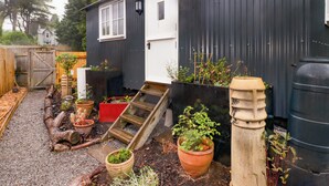A small house with a wooden deck, potted plants, and a water feature. - Kings Cwtch Shepherd's Hut (Cardiff)