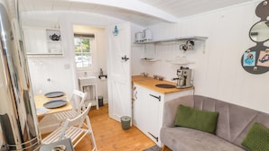 A compact kitchen with a dining area, a sofa, and a coffee machine. - Kings Cwtch Shepherd's Hut (Cardiff)