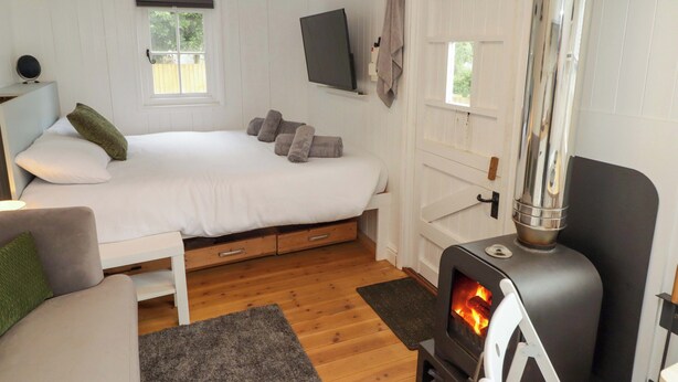 A cozy room with a bed, a sofa, a fireplace, and a TV mounted on the wall. - Kings Cwtch Shepherd's Hut (Cardiff)