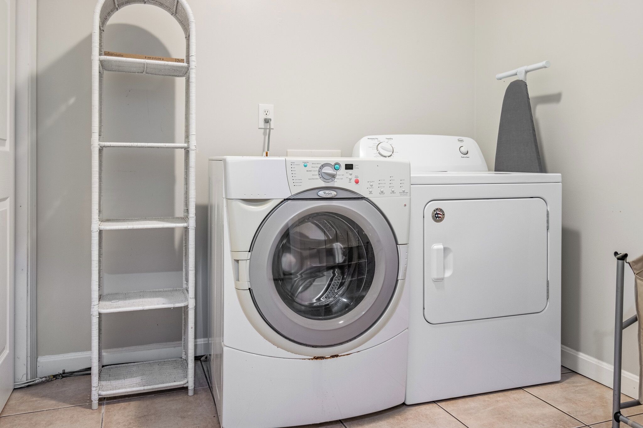 A laundry area with a front-loading washing machine, a drying rack, and a shelf unit.