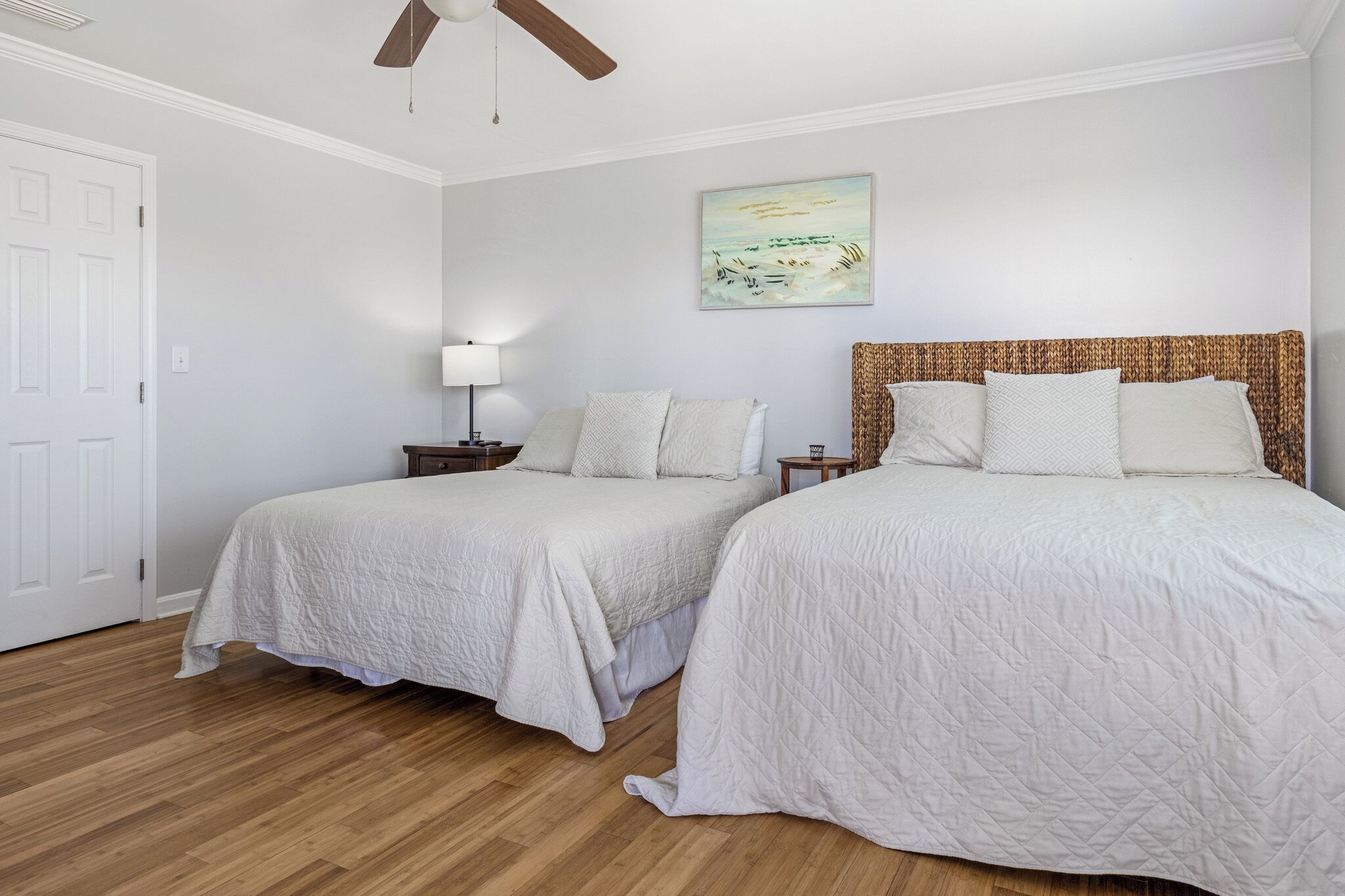 A bedroom with two beds, a ceiling fan, a nightstand with a lamp, and a painting on the wall.