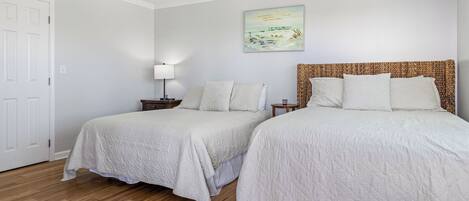 A bedroom with two beds, a ceiling fan, a nightstand with a lamp, and a painting on the wall.