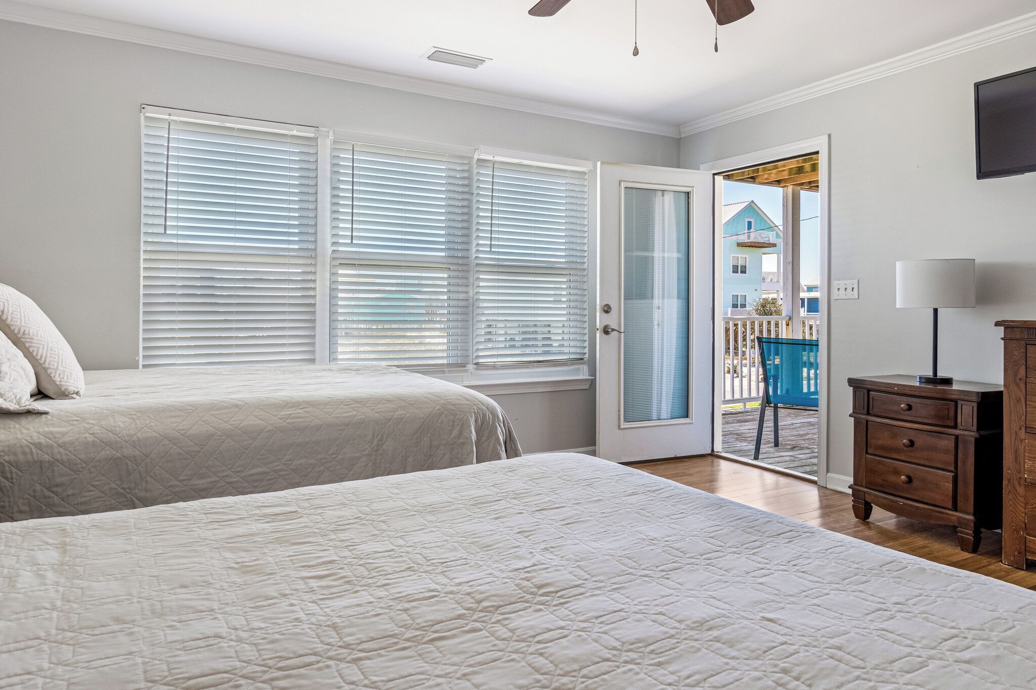 A bedroom with two beds, a wooden dresser, and a door leading to a balcony.