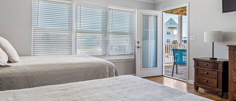 A bedroom with two beds, a wooden dresser, and a door leading to a balcony.