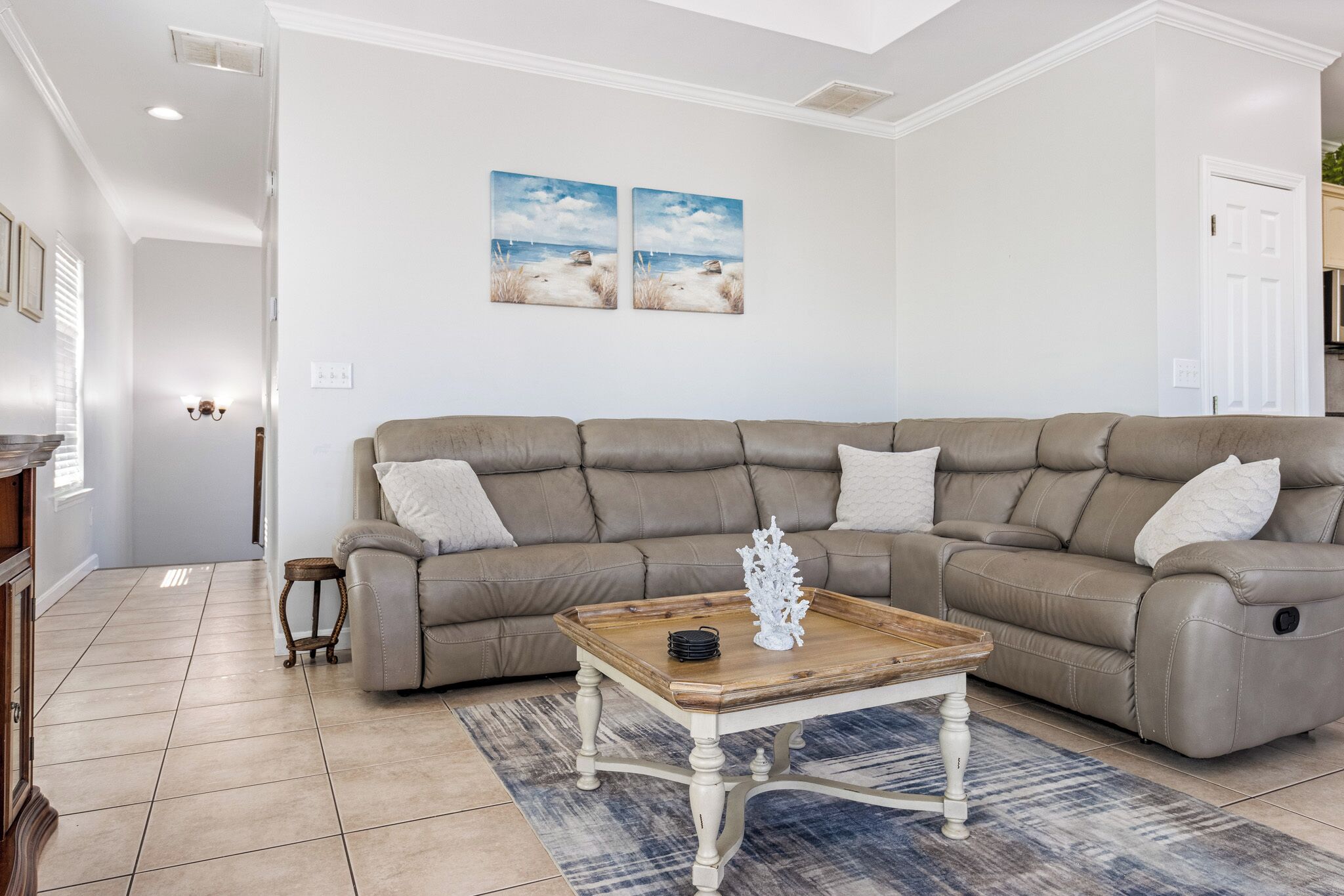A living room with a beige sectional sofa, a wooden coffee table, and two beach-themed wall art pieces.