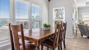 A dining area with a wooden table and chairs, a 'welcome' sign, and large windows with blinds. - Beach Memories by Southern Vacation Rentals (Gulf Shores)