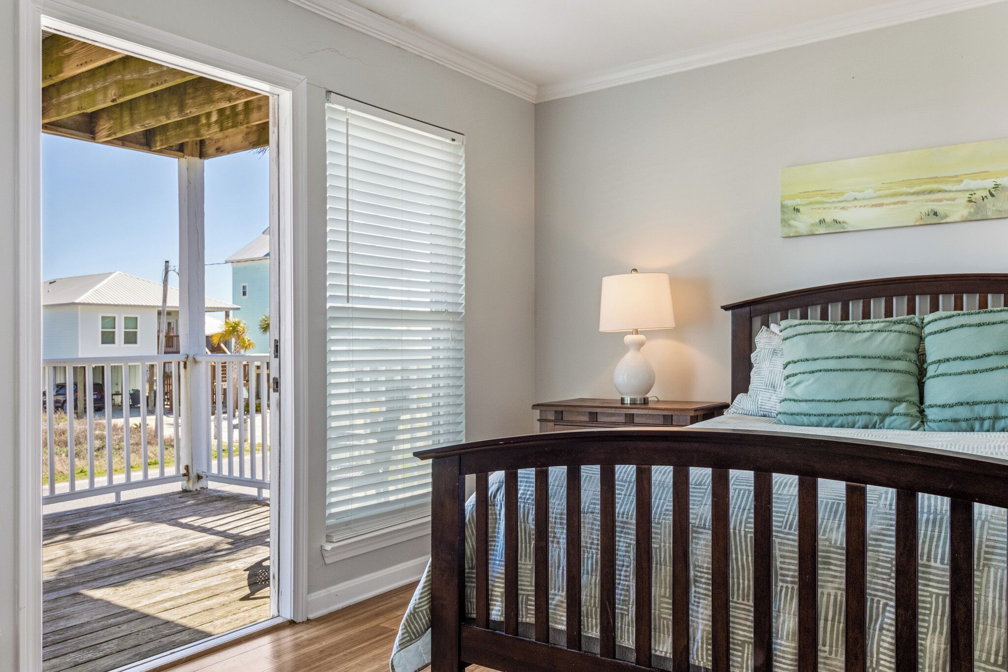 A bedroom with a wooden bed, a nightstand with a lamp, and a view of a balcony with a railing.