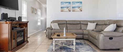 A living room with a sectional sofa, a wooden coffee table, a flat-screen TV, and a cabinet with speakers.